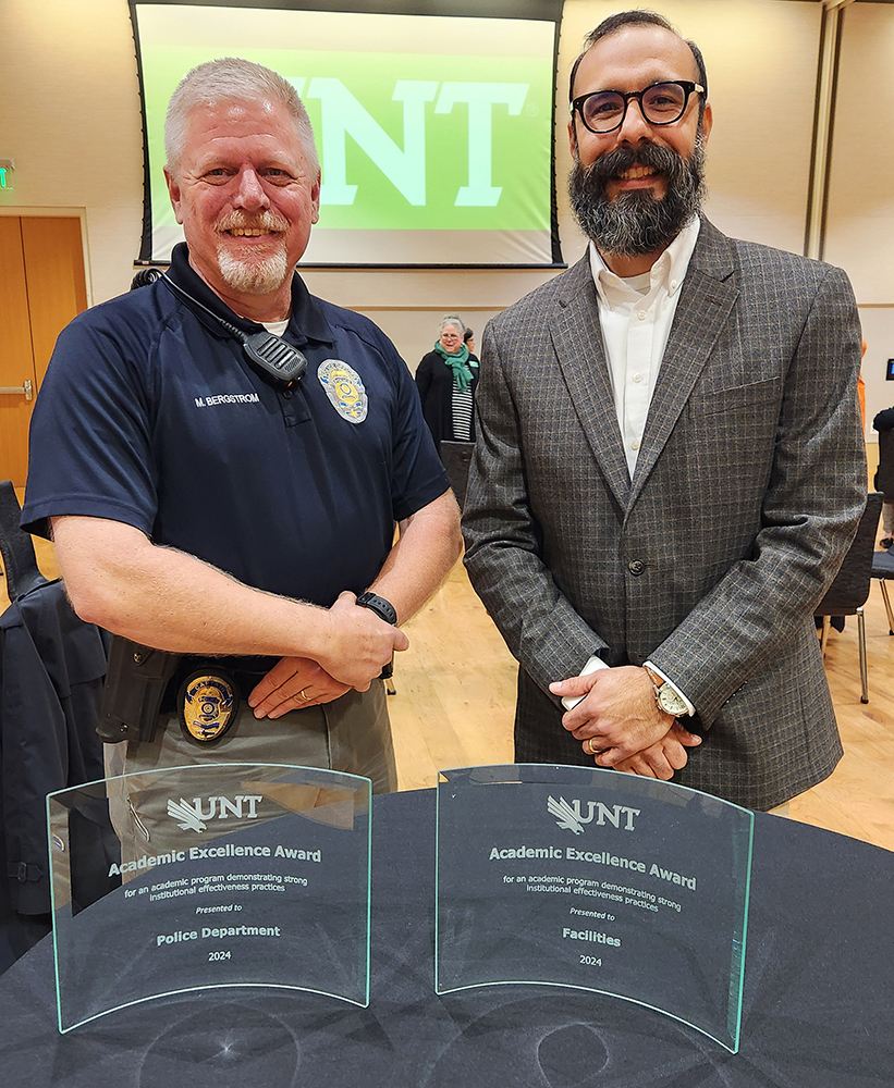 Department representatives stand in front of a table that includes awards for police and facilities departments.