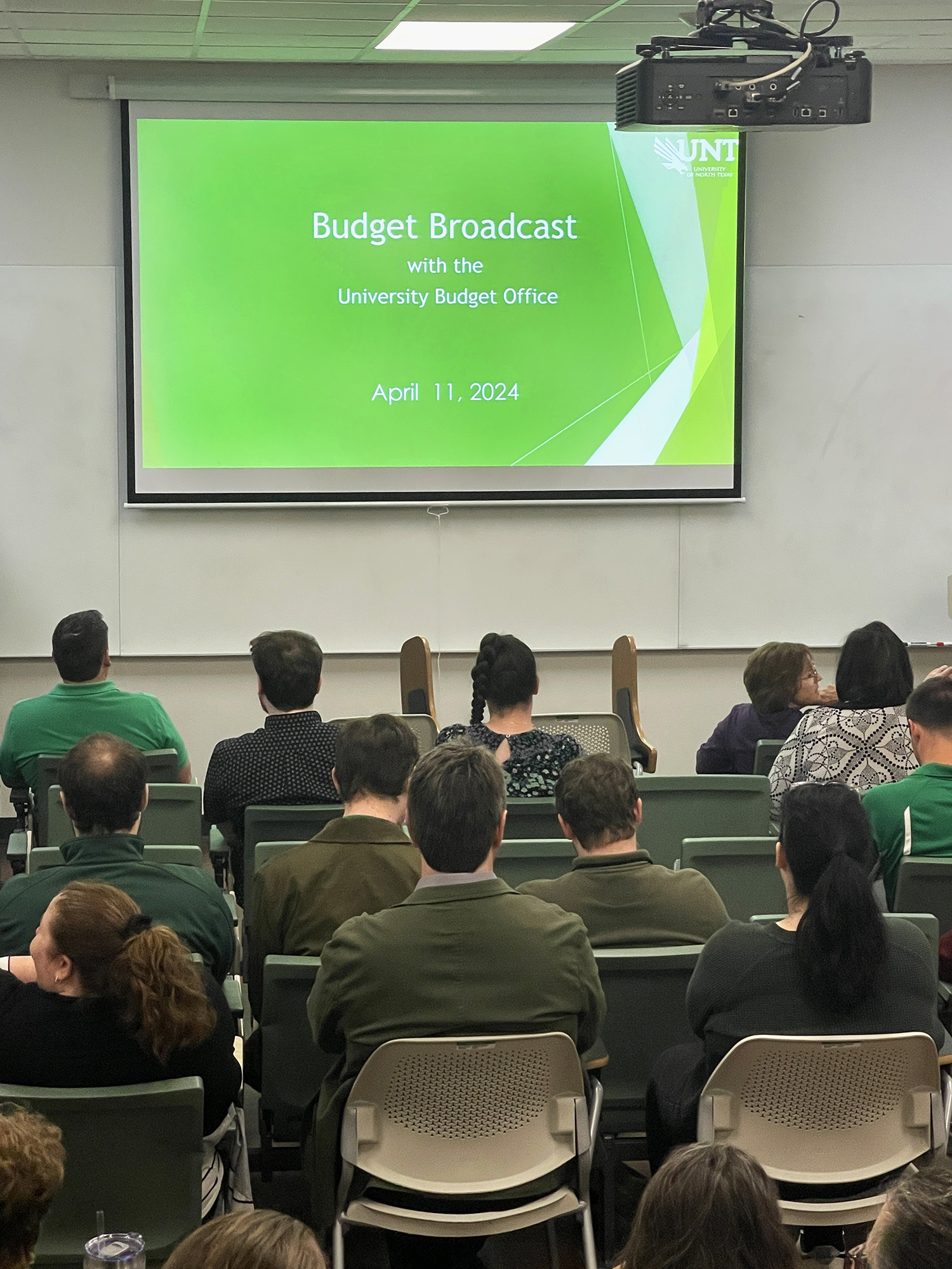 people sitting in a room looking at a slide that reads Budget Broadcast