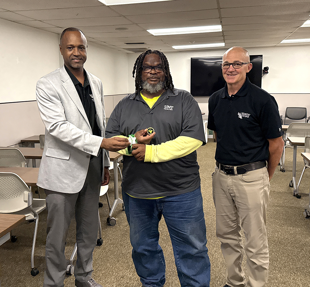 Clayton Gibson hands a coin to staff member James Taylor as Facilities director Jeff Brown looks on