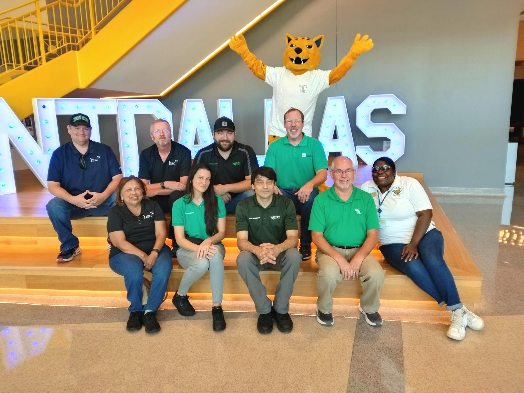 Asset Management team members sit on steps next to UNT Dallas sign