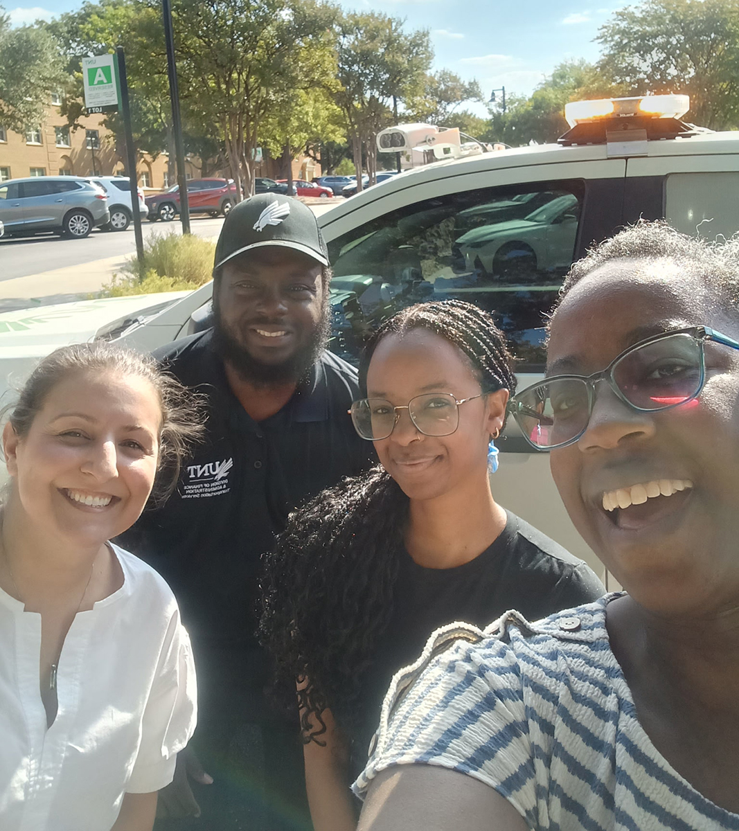 three members of the president's office standing in front of a truck with a parking staff member