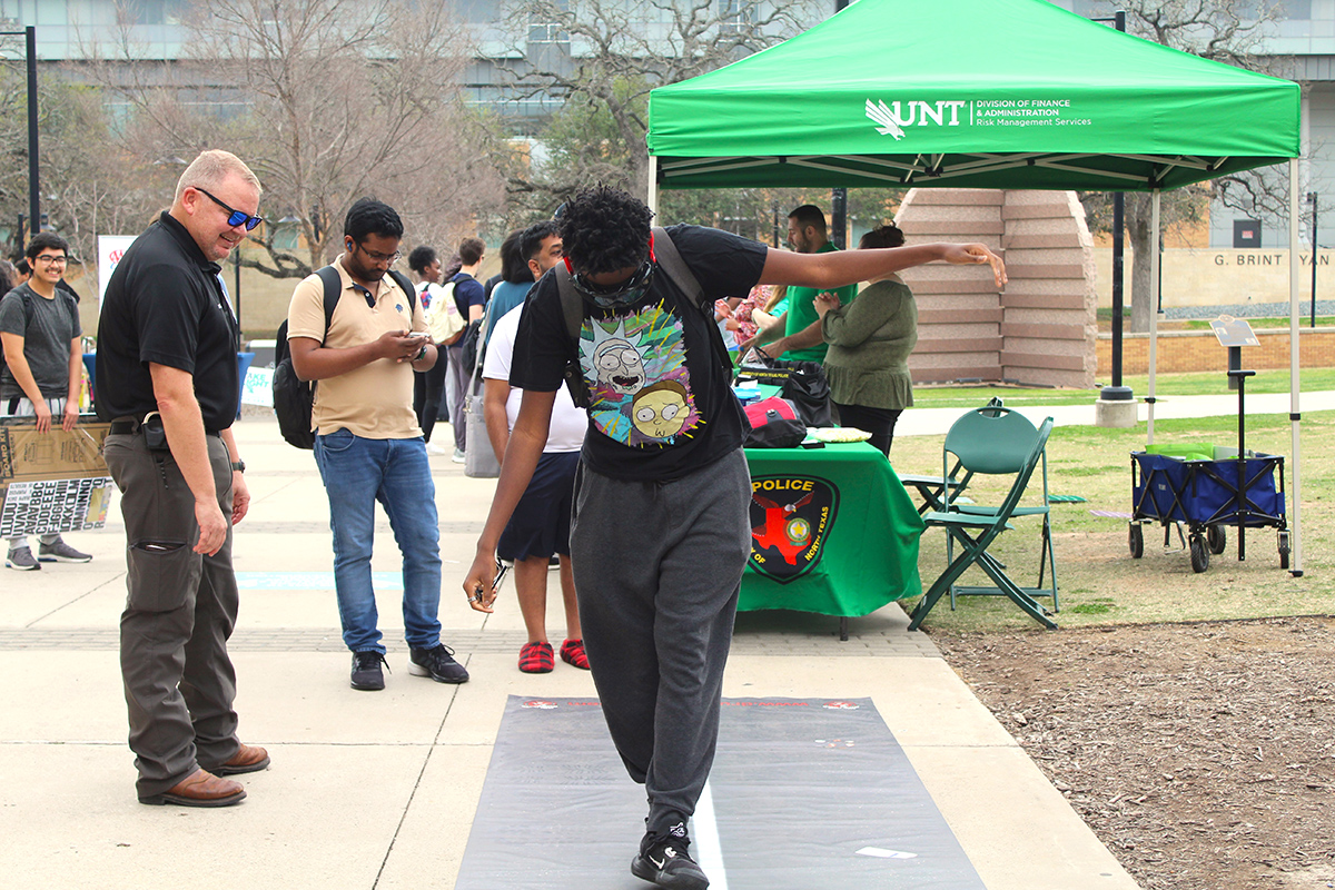 police officer watching a student trying to walk a straight line while wearing "drunk goggles"